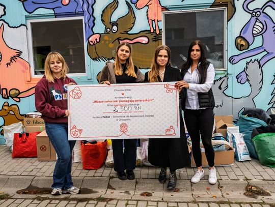 Cztery kobiety trzymają czek na 2500 zł przed budynkiem schroniska PsiKot; obok stoją przekazane dary